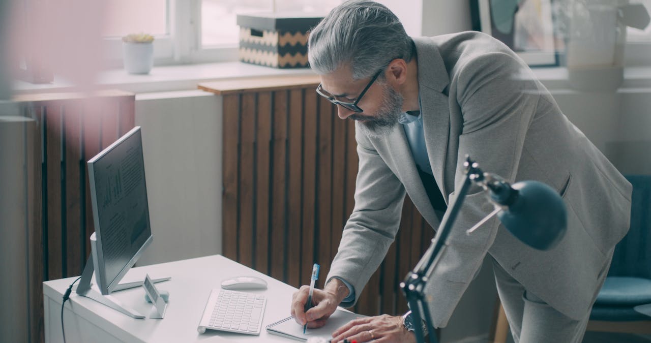 Businessman in suit writes at his desk in a modern office setting.