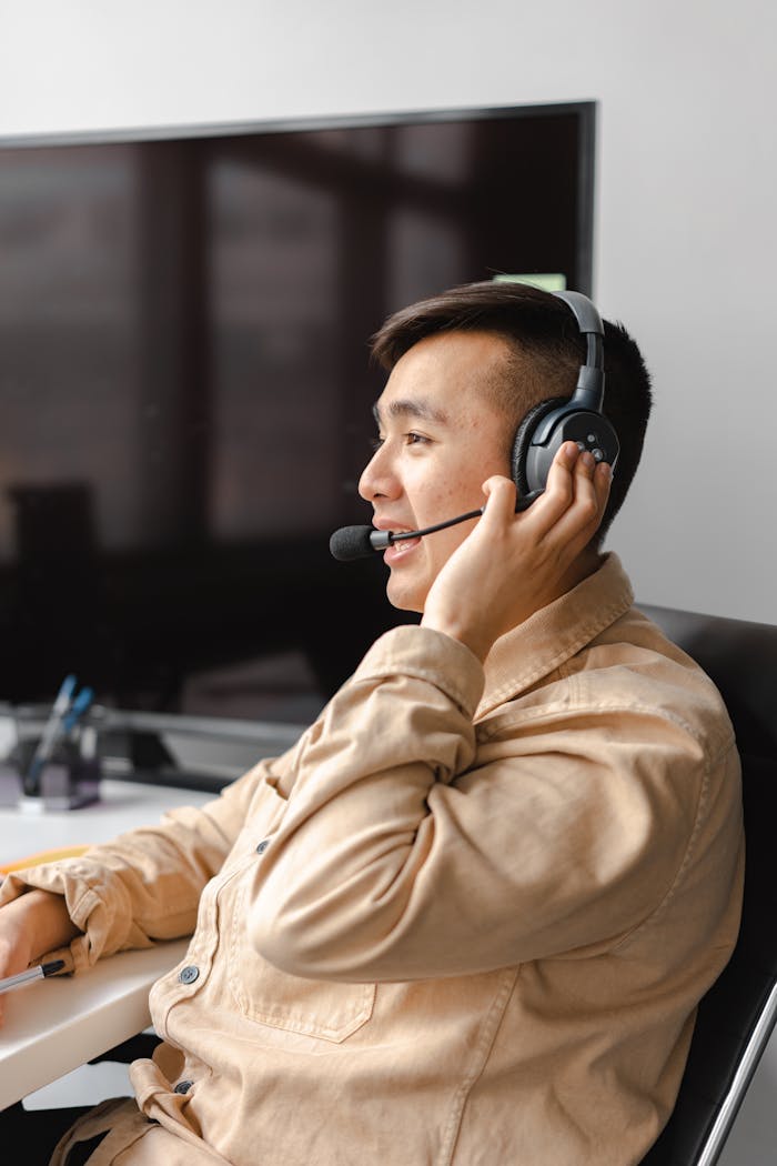 Asian man wearing a headset while talking, positioned in a modern office space.